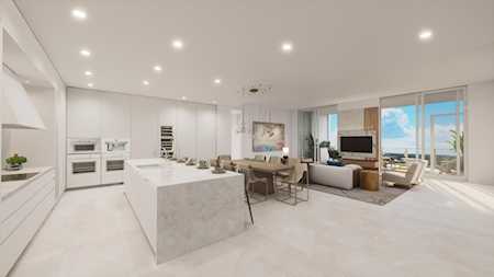 Open-plan white kitchen with marble island and living area beside floor-to-ceiling windows overlooking water.