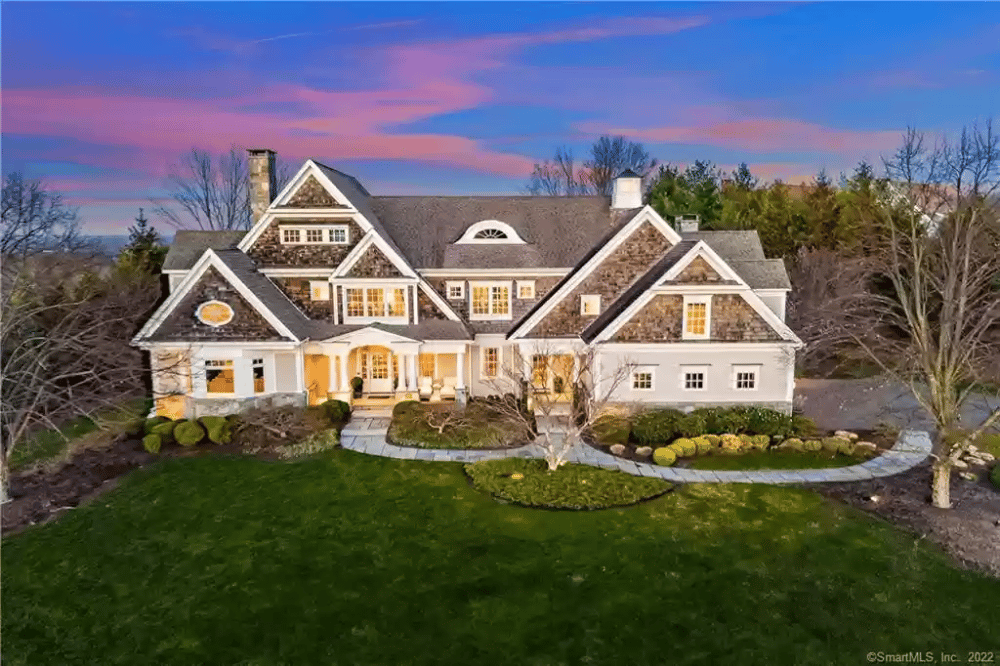 Large luxury home at dusk with stone accents, illuminated windows, and a curved front walkway.