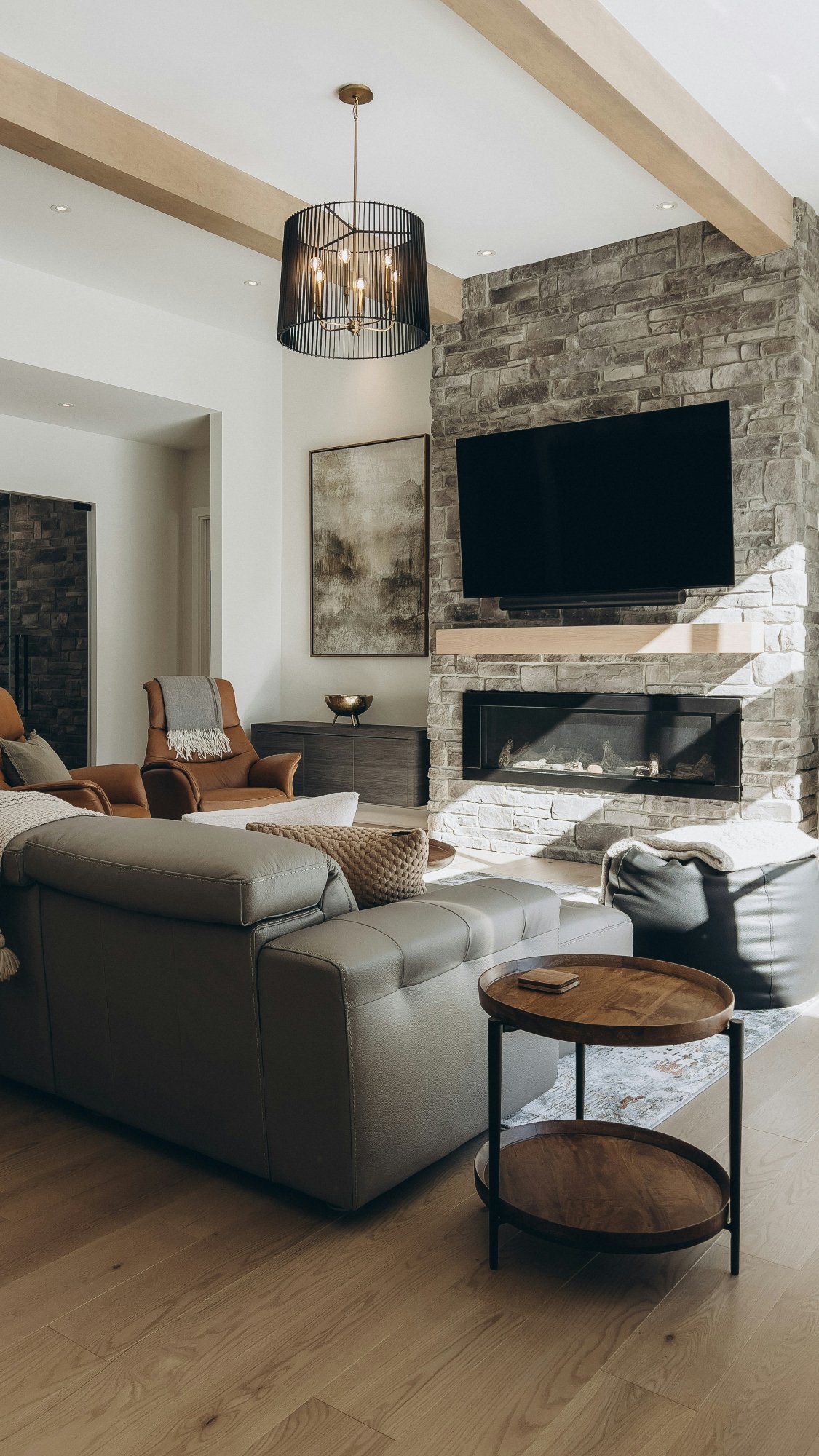 Living room with a stone fireplace, mounted television, exposed beams, and leather seating.