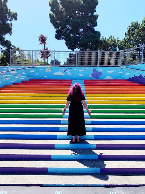 Woman standing on colorful rainbow-painted staircase mural in San Francisco park