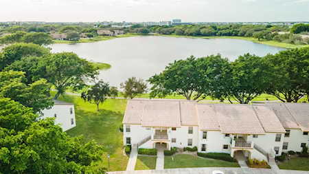Attached white homes beside a tree-lined lake, seen from above.