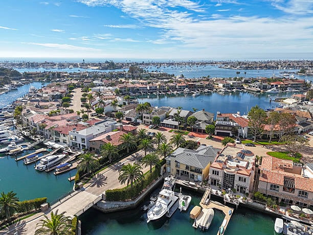 Aerial view of luxury waterfront homes in Newport Beach California with sailboats in the harbor, representing the high-end real estate market targeted by ultra-high-net-worth buyers in 2026