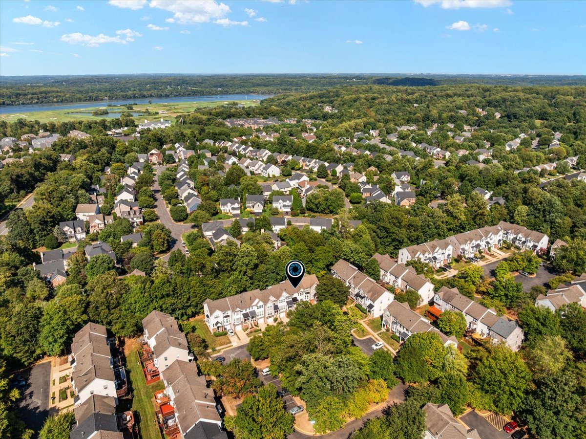Aerial view of townhomes amid dense trees, with a river in the distance and a marker over one home.