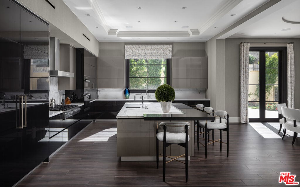 Modern kitchen with a large stone-topped island, dark cabinetry, and tall glass doors.