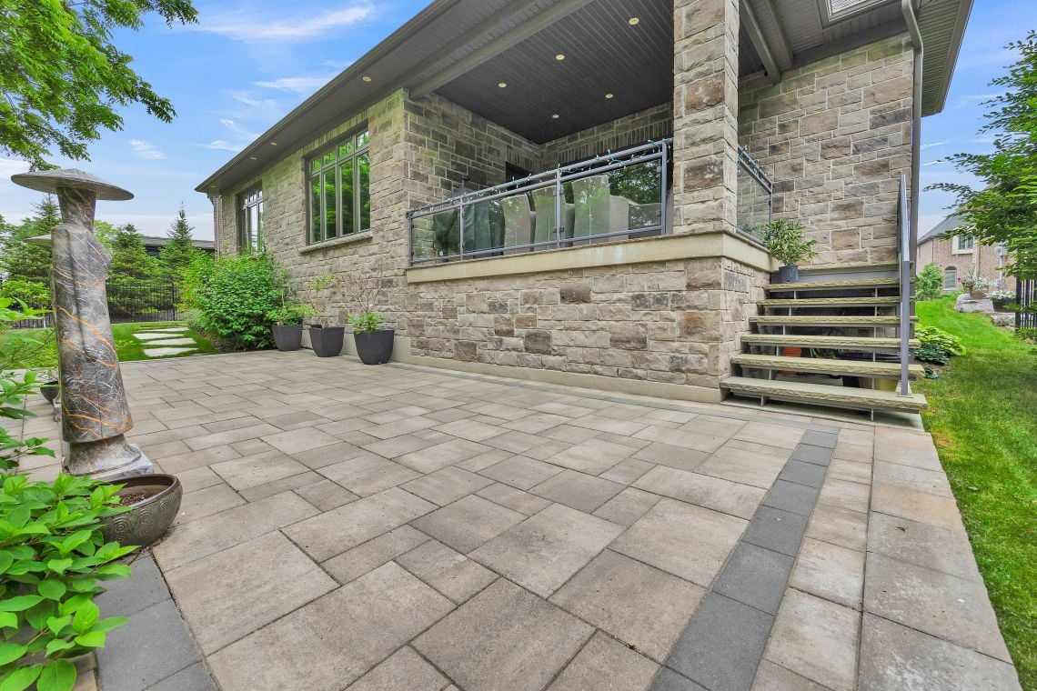 Stone house patio with broad paved terrace, glass-railed balcony, and landscaped garden.