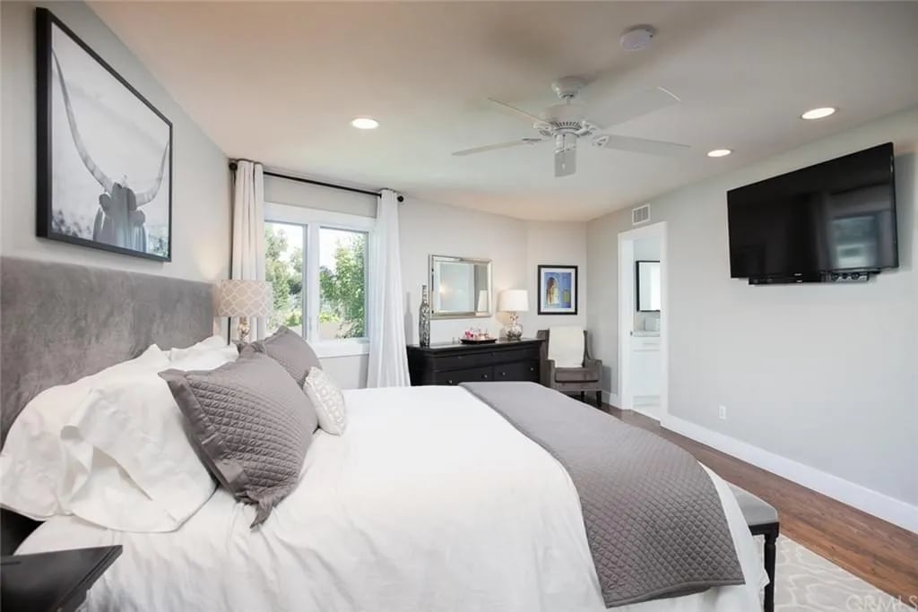  A comfortable bedroom with a large bed, a white ceiling fan, and a wall-mounted TV. A large framed photo of a longhorn is above the headboard.