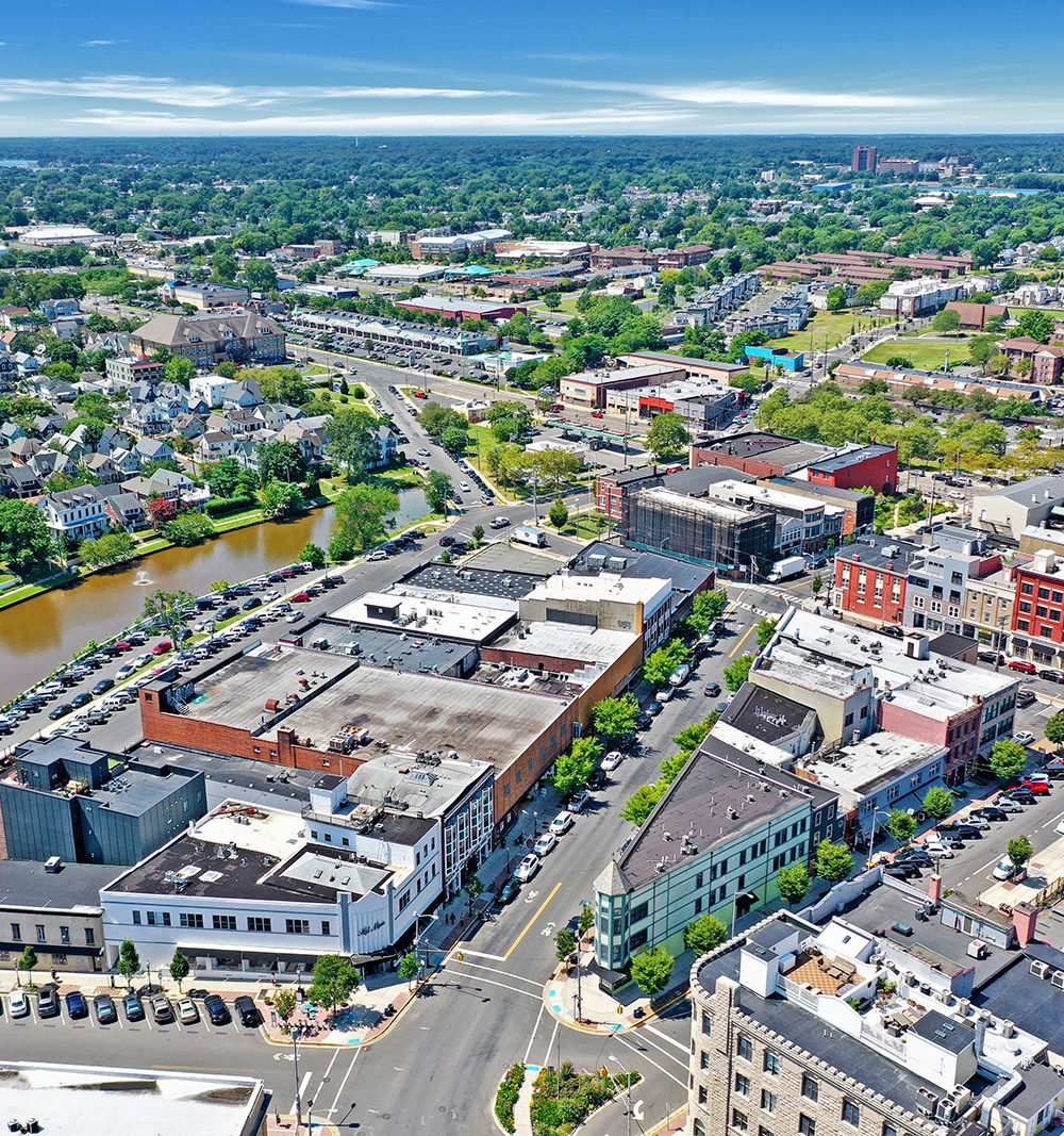 Aerial view of a downtown district with commercial buildings, intersecting streets, and trees on the horizon.
