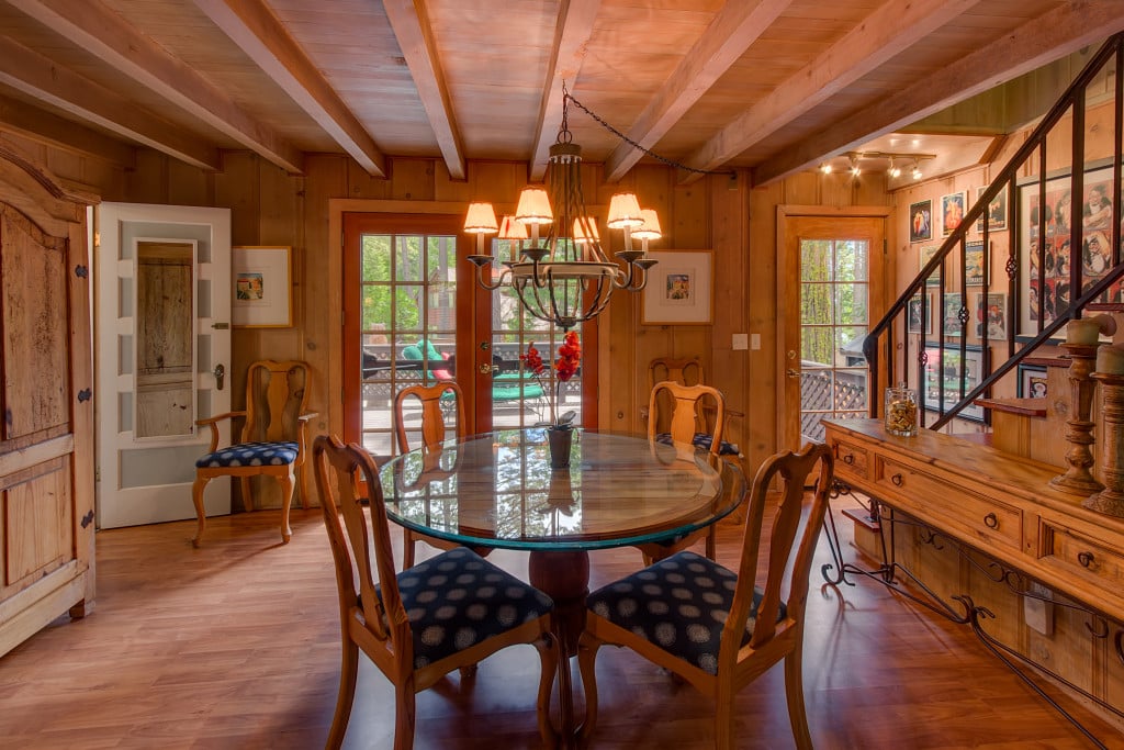 Wood-paneled dining room with an oval glass table, chandelier, and staircase lined with framed artwork.