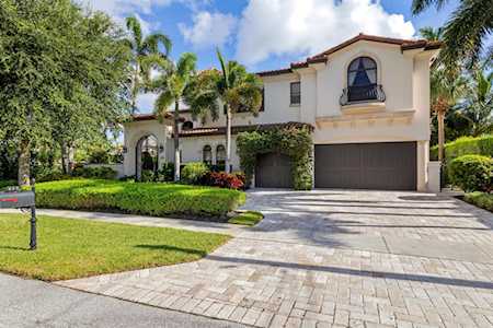 Two-story stucco home with arched windows, tropical landscaping, and a broad paved driveway.