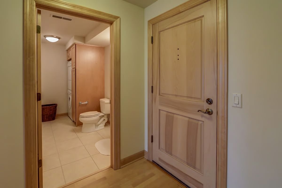 Entryway with a paneled wooden front door and an open view into the tiled bathroom.