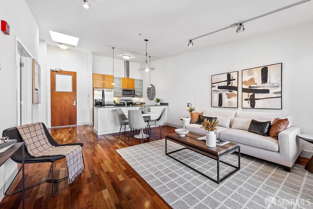 Open-plan living room with hardwood floors, a light sofa, and kitchen with wood cabinetry.