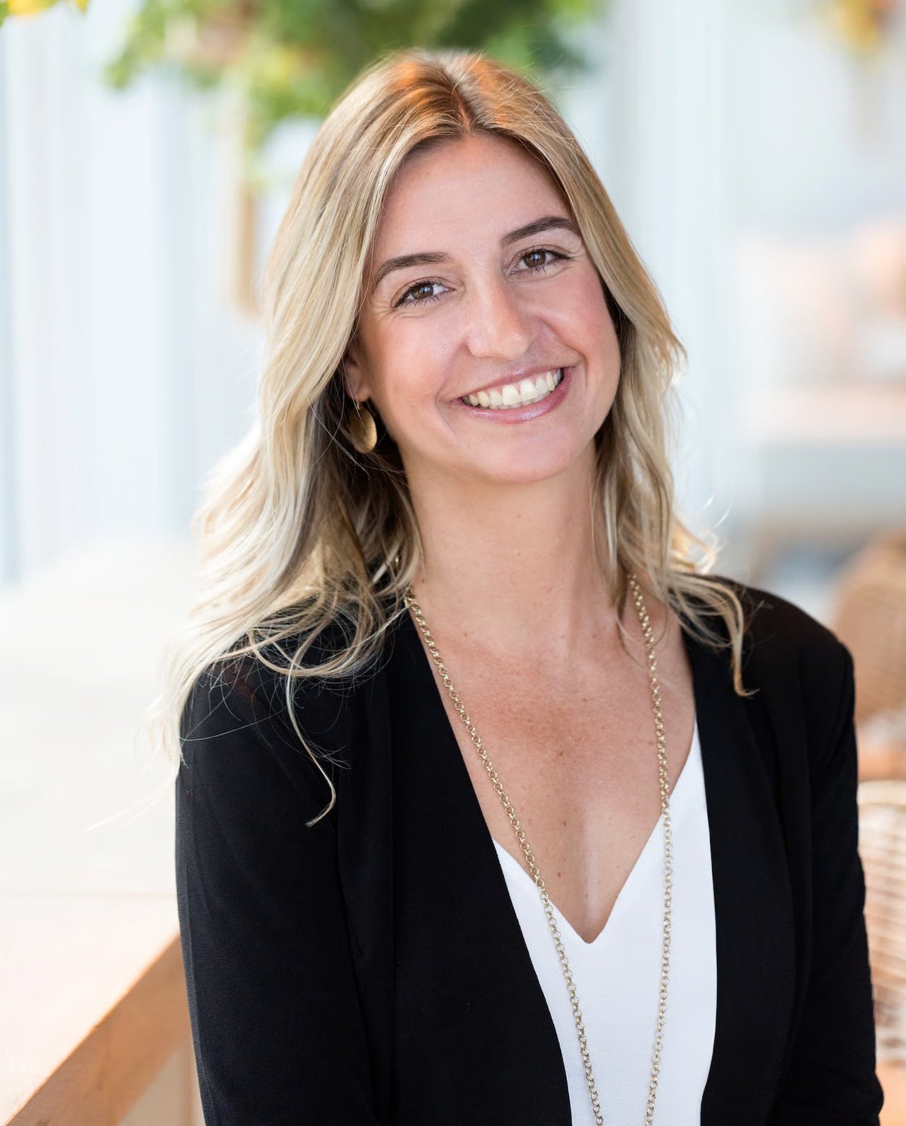 Kezia Ceccon smiling in a black blazer and white top, with long blonde hair and a gold necklace.