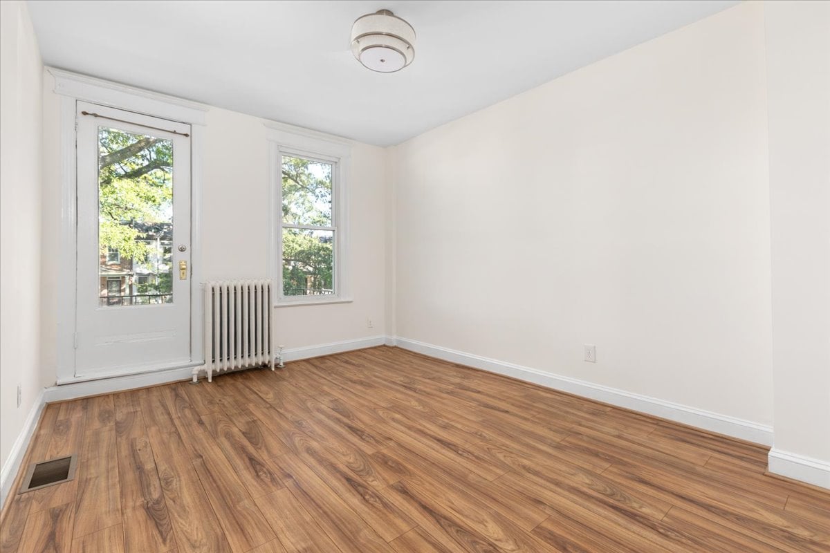 Empty room with wood-look flooring, a glass-paneled door, a window, and a radiator.