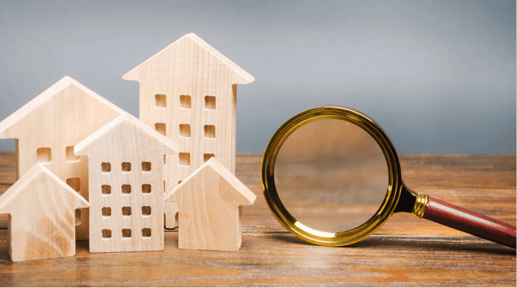 Wooden model houses beside a magnifying glass on a wooden surface.