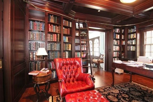 Wood-paneled library with built-in bookshelves, a red leather armchair, and a large desk.