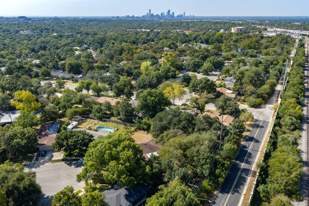 Aerial view of a tree-filled neighborhood with Austin’s skyline in the distance and railroad tracks along the right side.