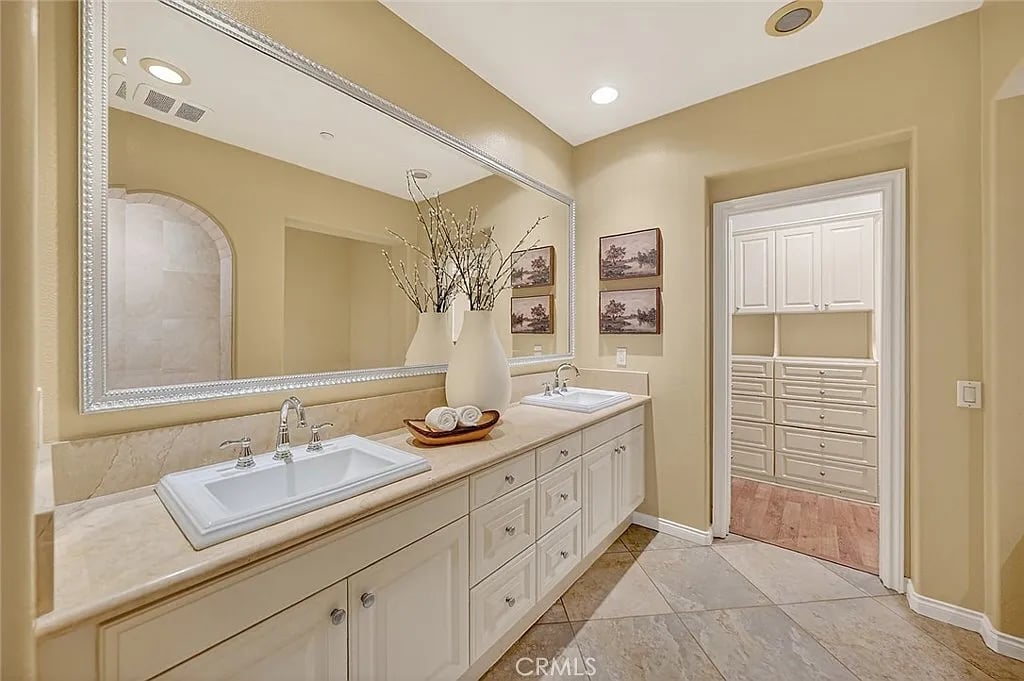 Bathroom with a double-sink vanity, large mirror, and doorway to a built-in dressing area.