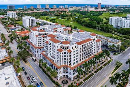 Aerial view of a white condominium complex with red tile roofs beside green space.