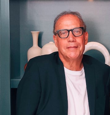 Ken Teitel wearing glasses and a dark blazer, seated before sculptural white vases.