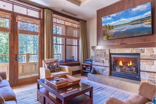 Living room with tall wood-framed windows, a stone fireplace, and a wall-mounted landscape display.