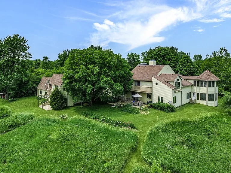 Large light-colored house with a screened porch, mature trees, and a broad green lawn.