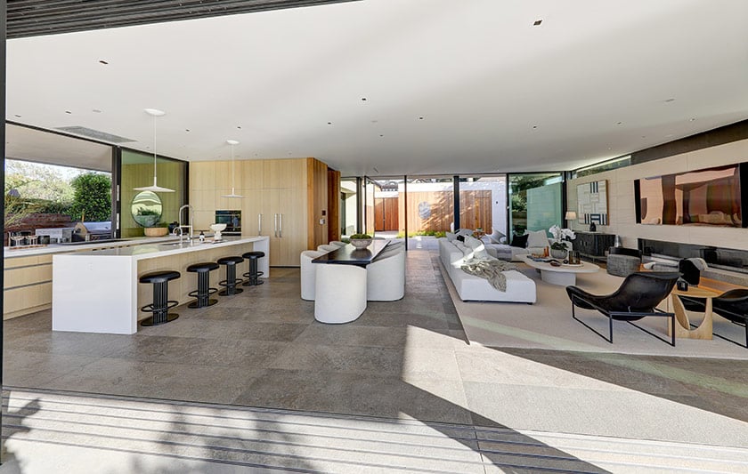 Modern open-plan kitchen and living room with pale wood cabinetry and a courtyard view.