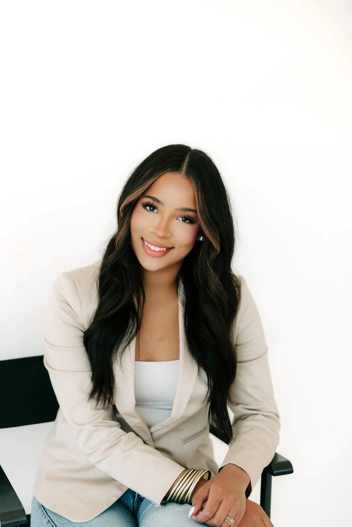 Mercy Chollett seated in a cream blazer, smiling against a white background.