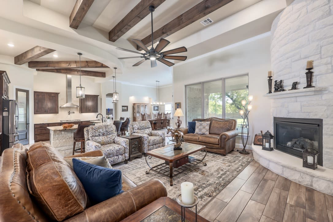 The home's elegant touches extend to the living spaces, where a stone fireplace adds warmth and charm, accented by trey ceilings with beams that extend seamlessly into the kitchen.