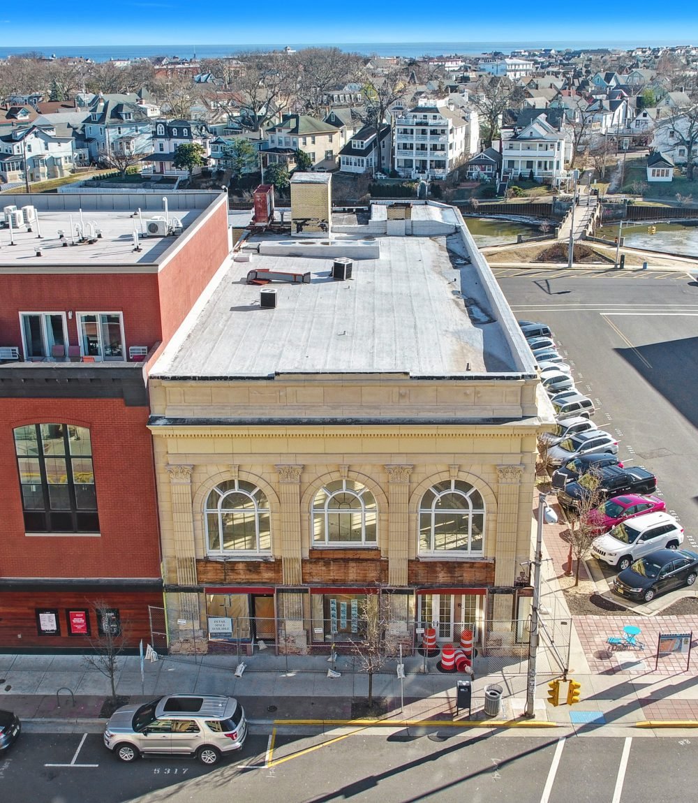 Aerial view of 574 Cookman Avenue, showing its cream facade, arched windows, and storefront construction barriers.