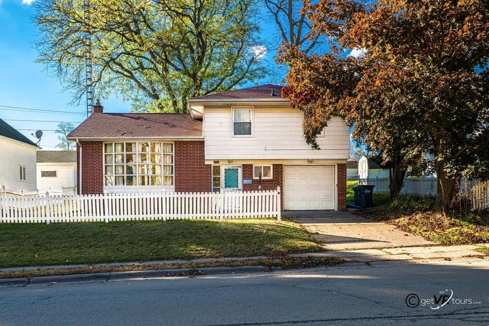 Two-story brick and white-sided house with a picket fence, bay window, and attached garage.
