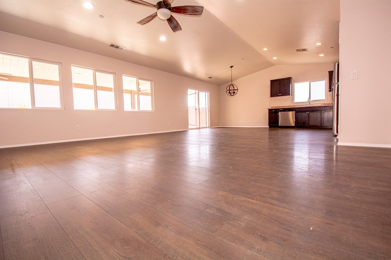 Vacant open-plan living area and kitchen with dark flooring, large windows, and dark cabinetry.