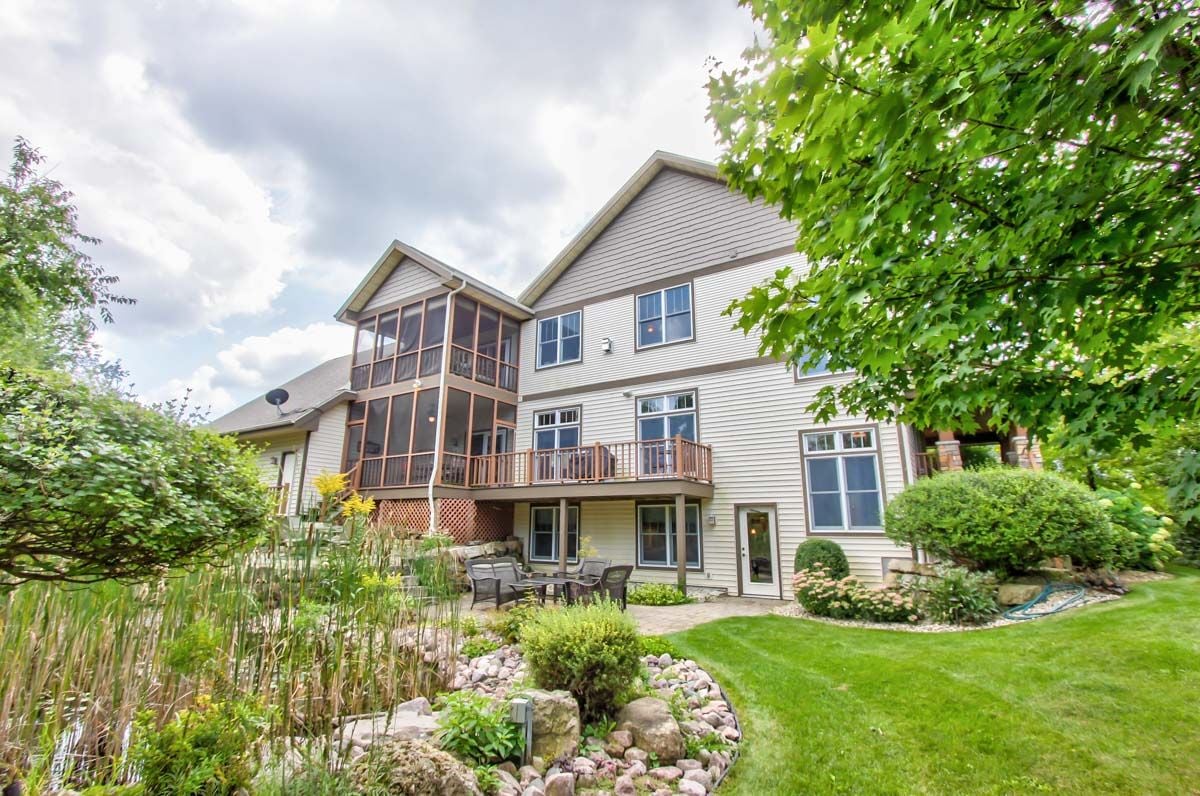 House with a raised deck and screened porch overlooking a landscaped garden and lawn.