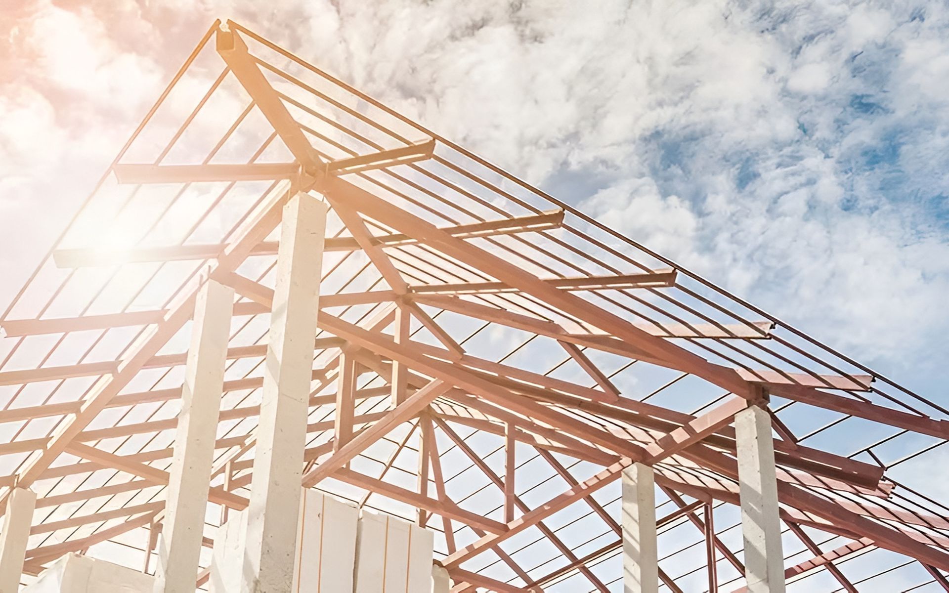 Unfinished building with exposed wooden roof trusses and concrete columns beneath a cloudy sky.