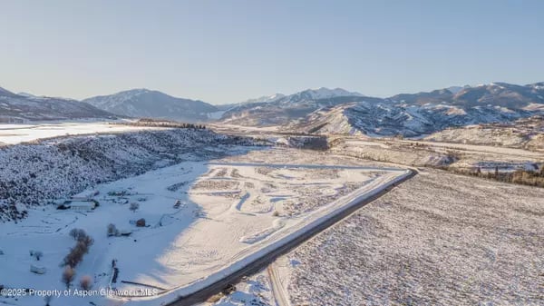 Aerial view of a snow-covered valley with a road and distant mountains.