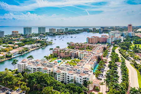 Waterfront neighborhood with condominium buildings along a broad waterway and tree-lined road.