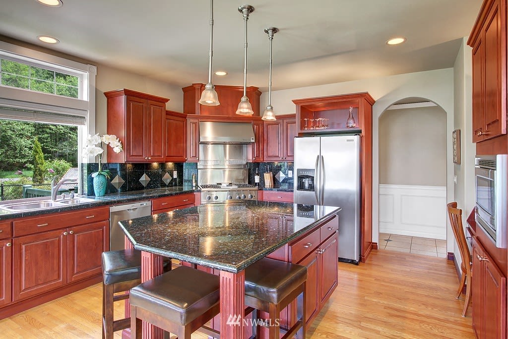 Kitchen with cherry cabinets, granite island seating, stainless steel appliances, and a large garden-facing window.