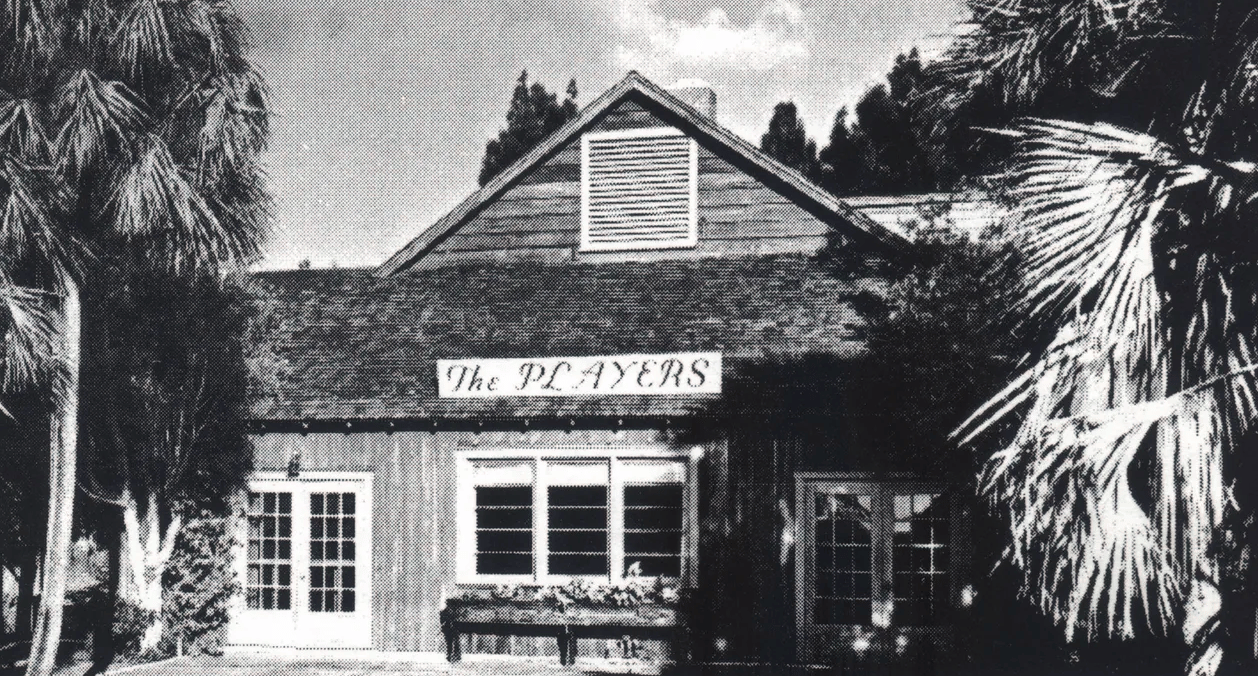 Wood-sided building marked “The PLAYERS,” framed by palm trees.