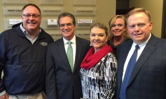 Five adults pose together in front of Benchmark Realty signage.