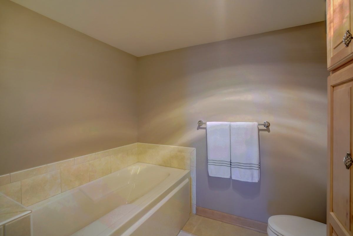 Bathroom with a built-in soaking tub, cream tile surround, and white towels on a wall rack.