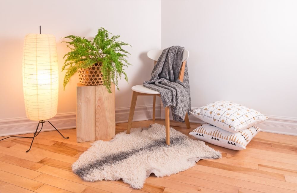 Styled room corner with a paper floor lamp, fern, draped chair, patterned cushions, and fluffy rug.