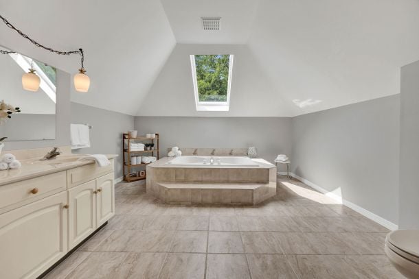 Spacious bathroom with a freestanding tub beneath a skylight and a long cream vanity.