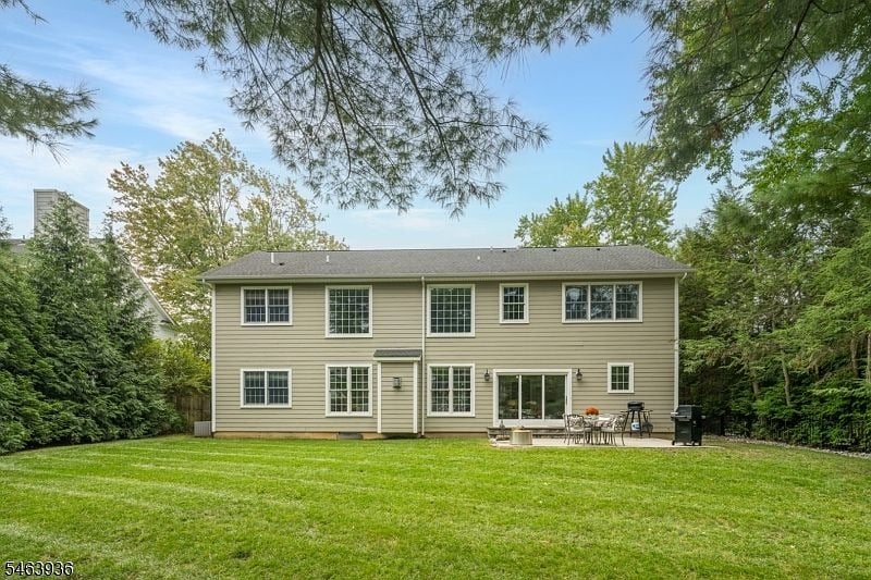 Rear of a two-story beige house beyond a broad lawn, with patio furniture and mature trees.