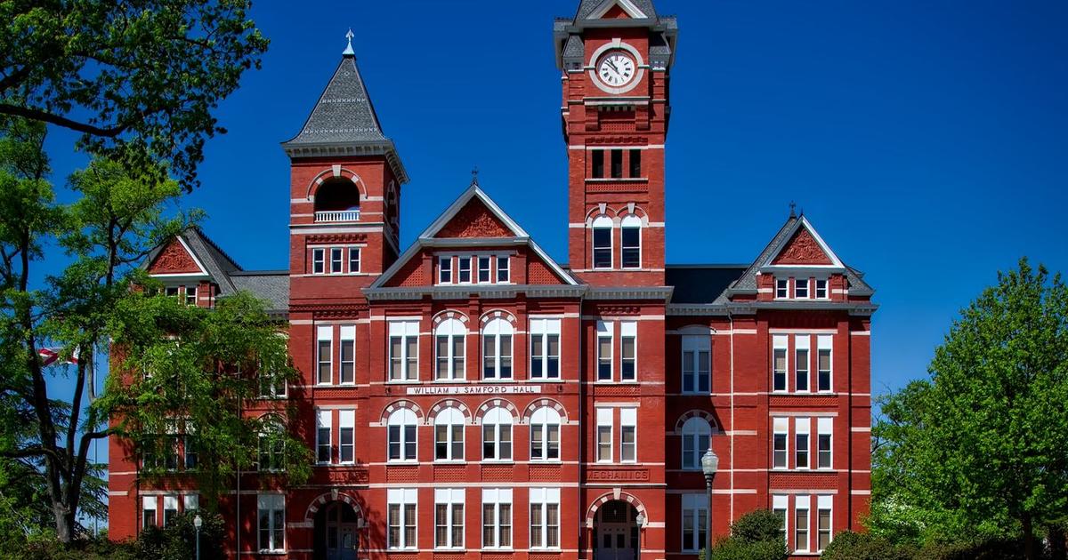 Samford Hall, the red brick clock tower building on the Auburn University campus in Auburn, Alabama, under a clear blue sky.