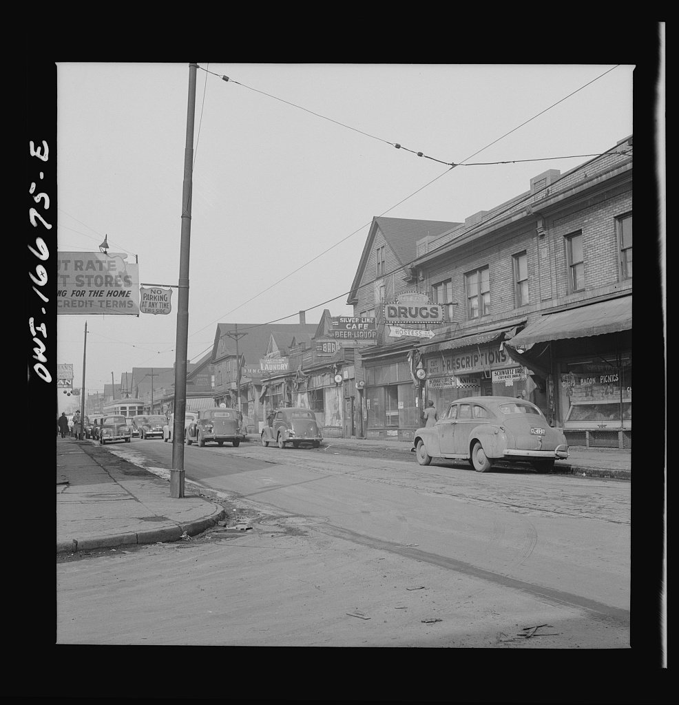 Historic commercial street with brick storefronts, parked cars, and overhead wires.