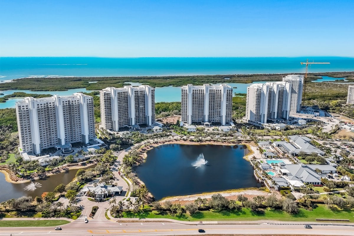 Aerial view of Kalea Bay showing five completed towers in a row above the community lake, with the mangrove estuary and the Gulf of Mexico beyond.