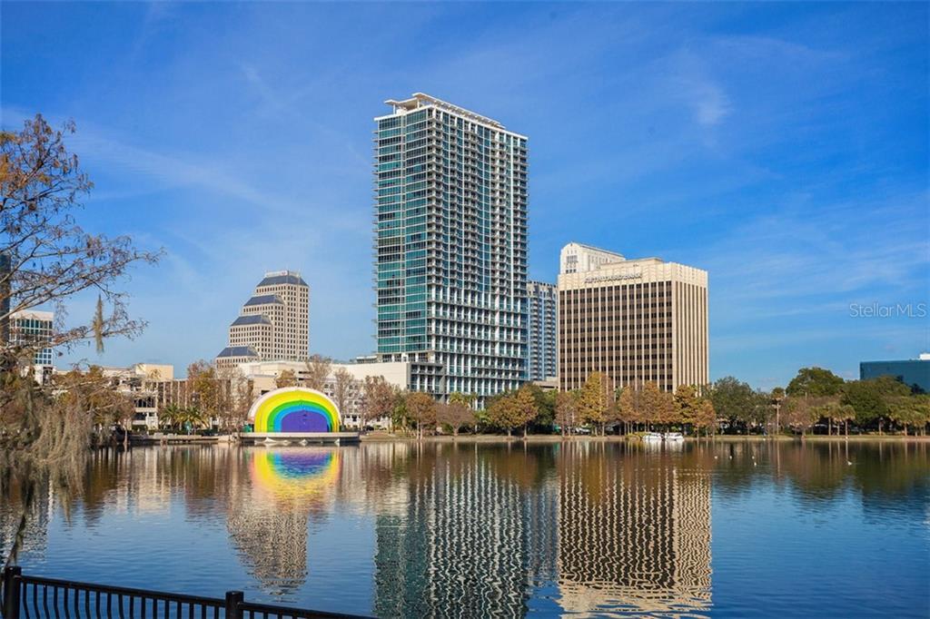 Downtown Orlando skyline reflected in Lake Eola, with a glass residential tower and rainbow sculpture.