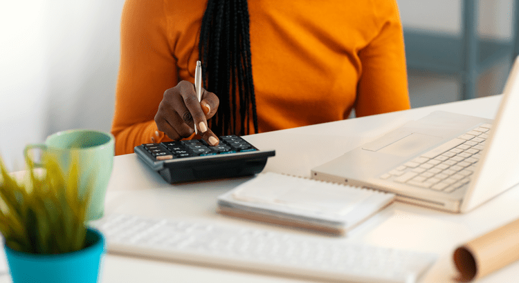 A woman seated at a desk, using a laptop and a calculator for work or study purposes.