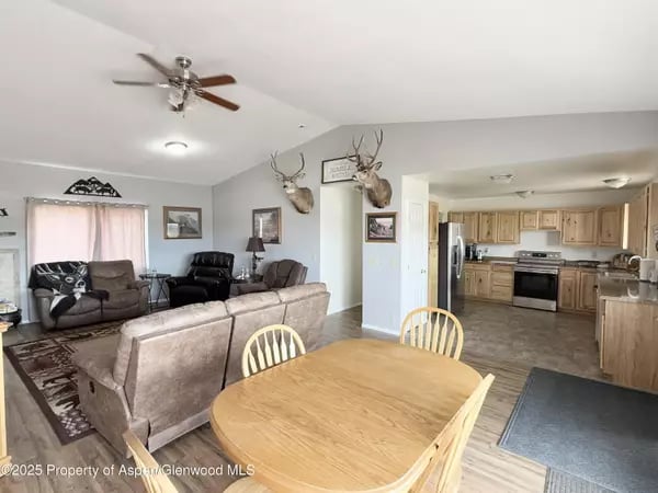 Open-plan living and dining room with a round wooden table, upholstered seating, and an adjoining kitchen.