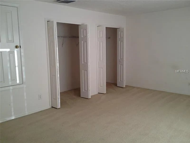 Empty carpeted room with two open closets and a white paneled door.