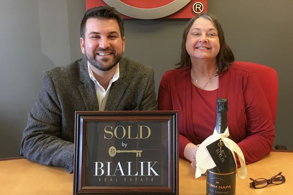 Two people celebrate a home closing behind a SOLD by Bialik Real Estate sign.